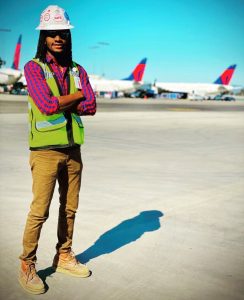 DeAndre standing on a runway wearing a hard hat with planes in the background.